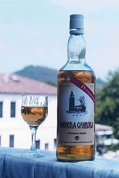 Bottle and glass with ambre colored rakija on a balcony reeling with buildings in the background