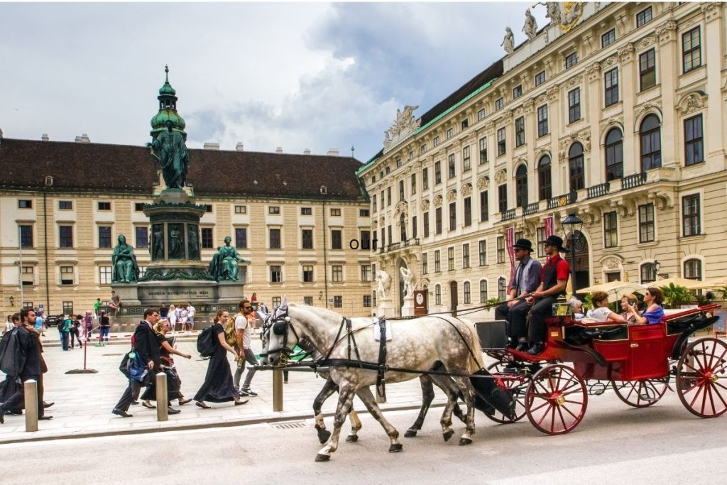 Red horse carriage with white horse in front of classic architecture building in vienna austria