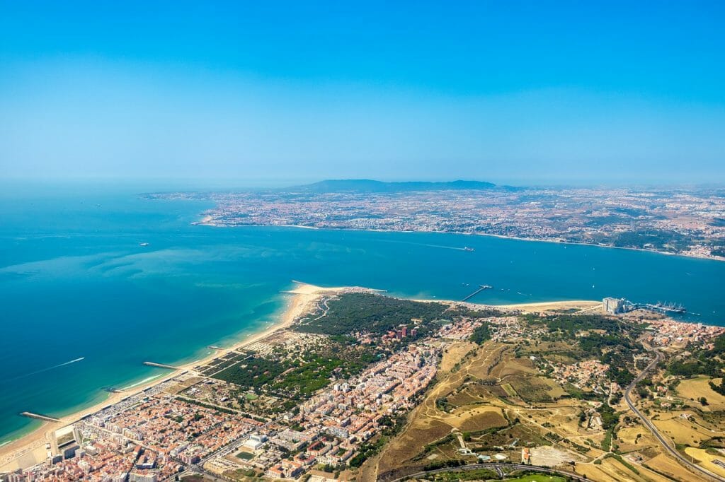 Birds eye view over costa da caparica near Lisbon, showing turquoise and blue water and yellow sand beaches.
