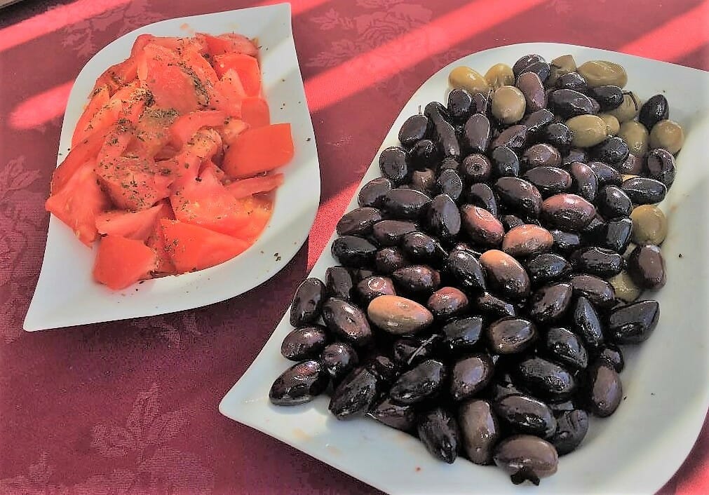 Santorini Day Tours exposed us to delicious Tomatoes and Greek Olives in separate white dishes on a red table cloth