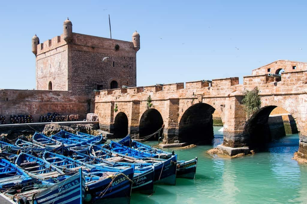 Blue boats in front of medieval bridge and tower in Essaouira Game of Thrones Film Location in Morocco 