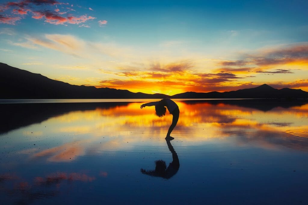 Woman doing a backbend on a beach at sunset