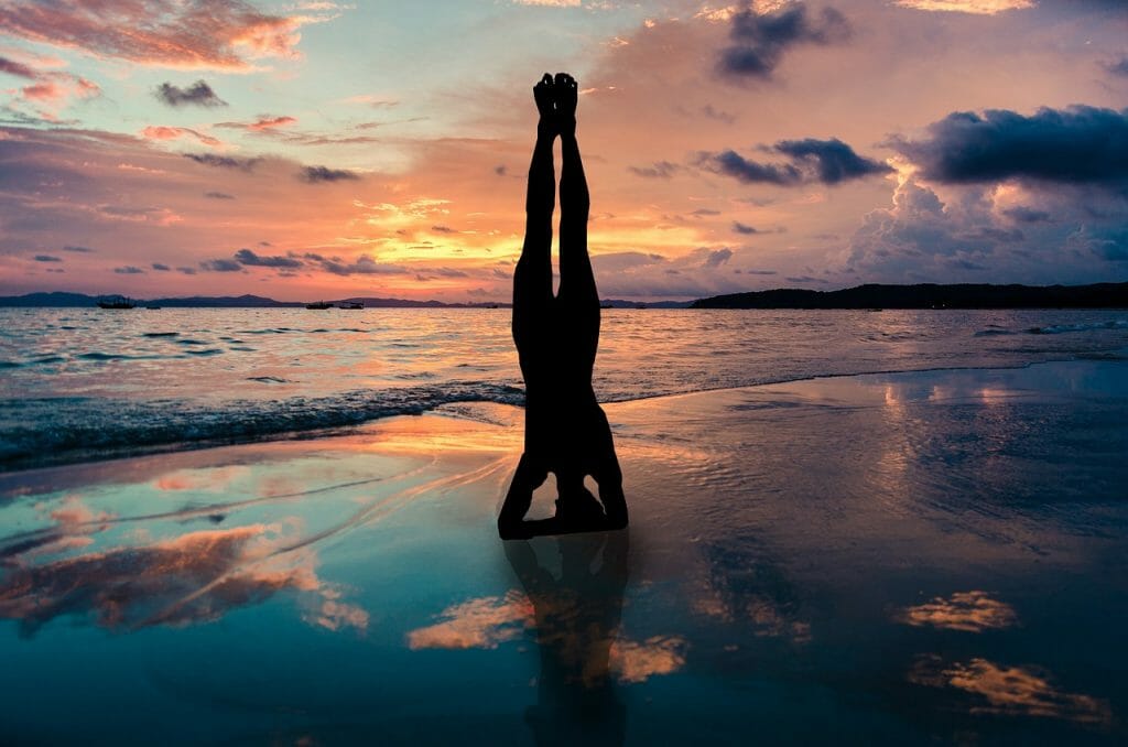 Woman doing handstand on the beach during sunset