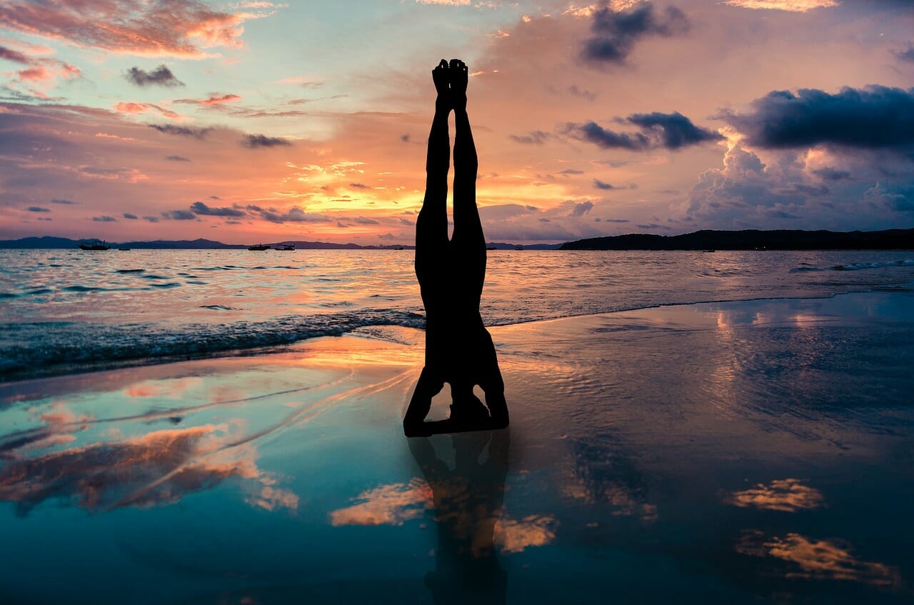 Woman doing handstand on the beach during sunset