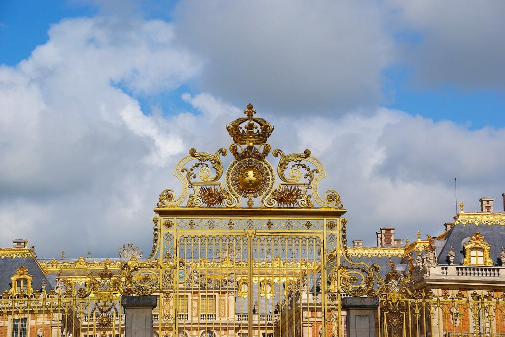 The golden Palace of Versailles in front of a cloudy, blue sky