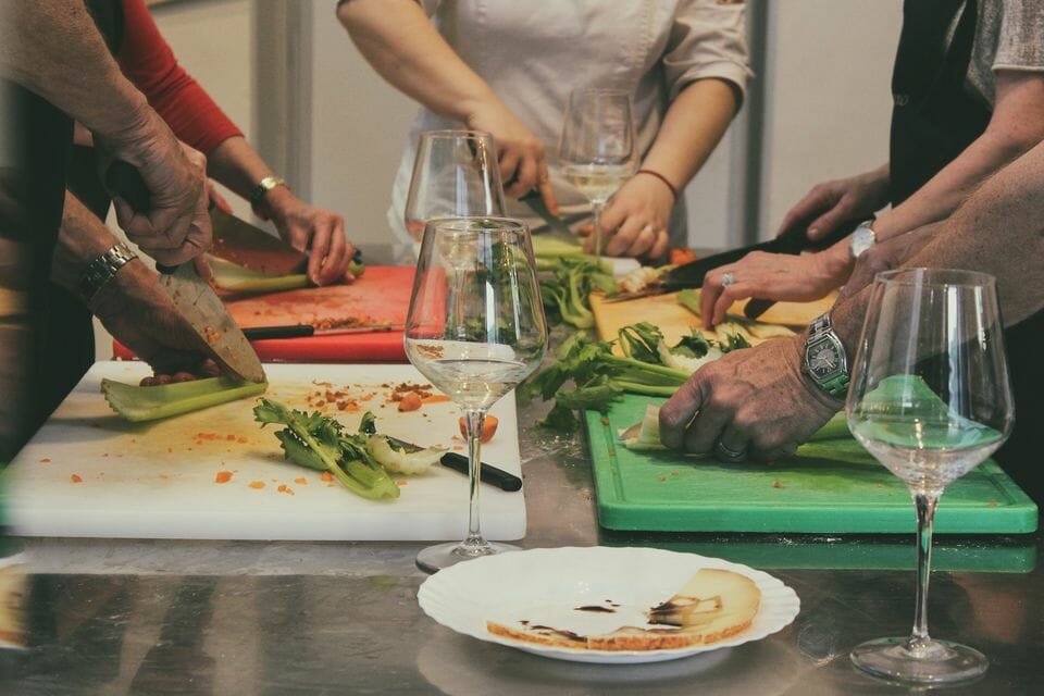People around a table, chopping vegetables with wine glasses