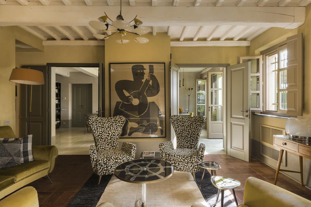 Inside of a suite at the Hotel Locanda al Colle with a painting of a guitar player, print chairs, and natural light