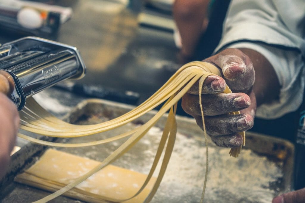 Chefs hands roll cutting fresh linguini with flour dusting his hands