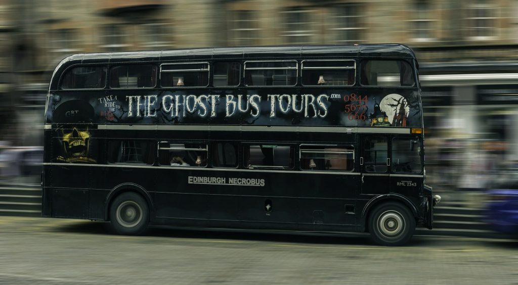 Black double decker ghost tour bus with the Edinburgh logo on the side, speeding down the street