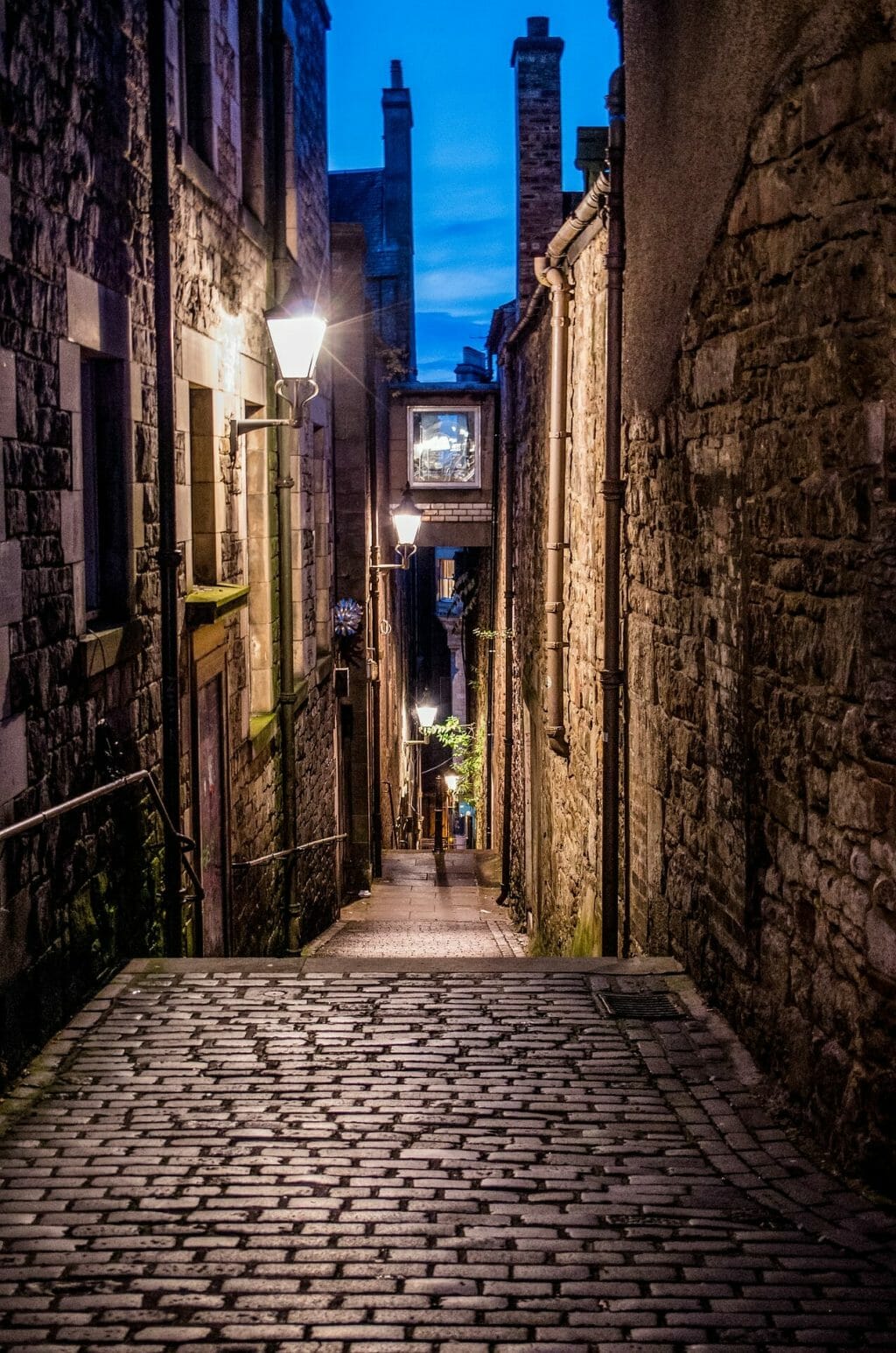 Cobblestone alley in Edinburgh in the evening with a lamp glowing with light