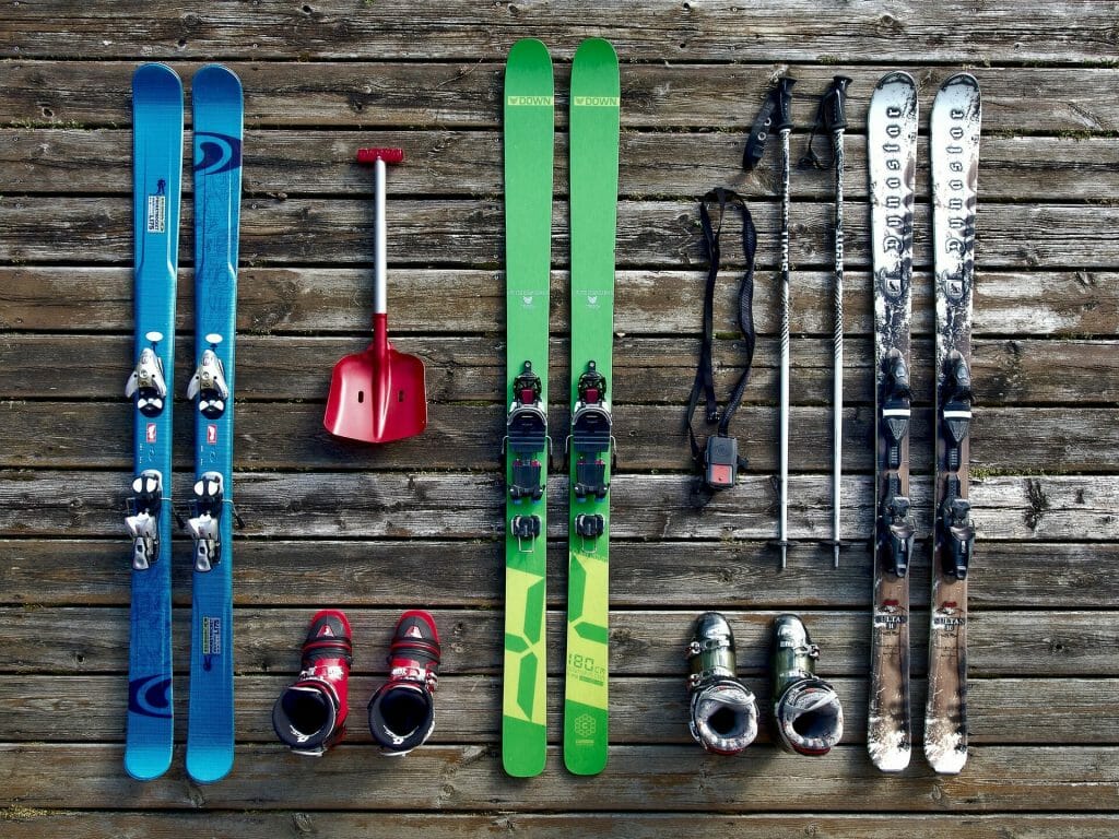 Blue and green skis laid out on the floor with their poles by their sides