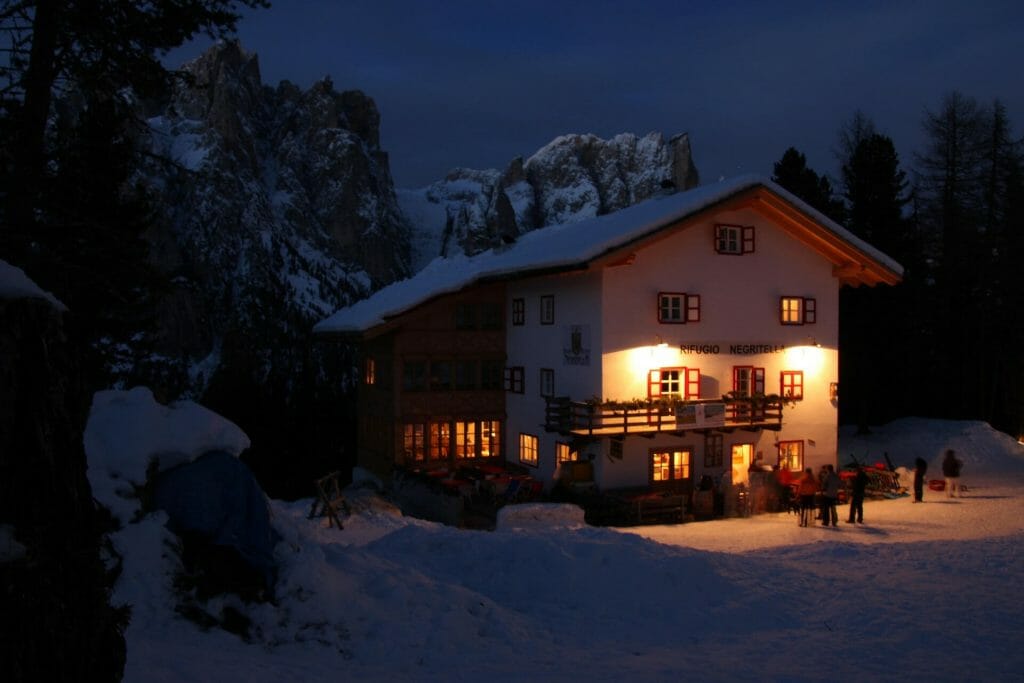 Ski cabin glowing in the winter night with people mingling around