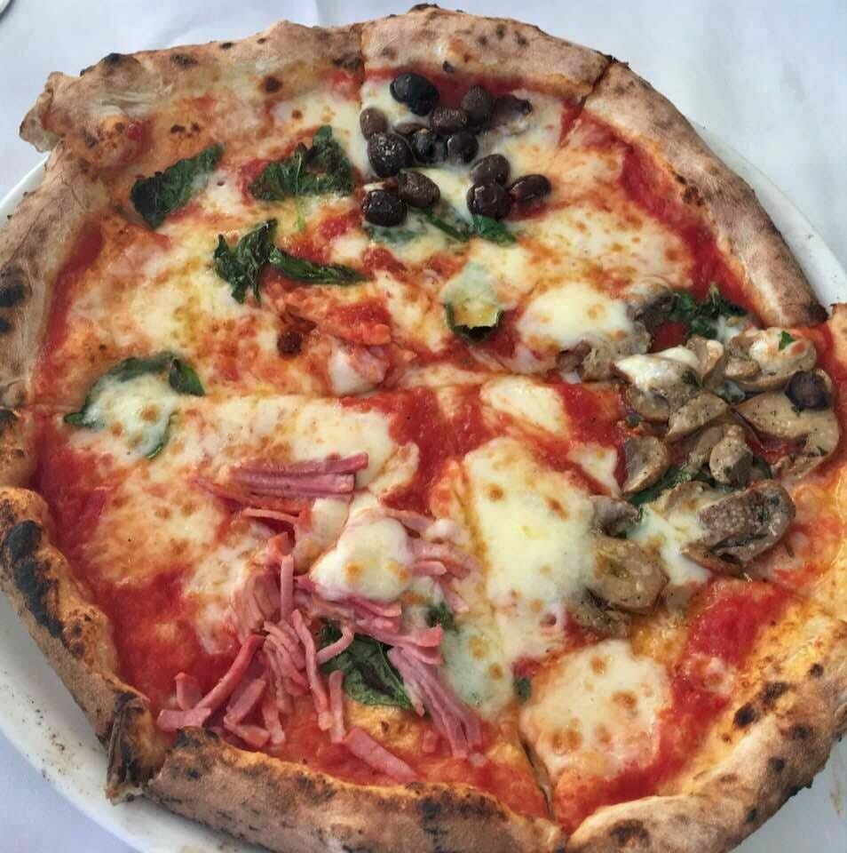 Pizza divided into four parts with olives, mozzarella, ham, basil, and mushrooms