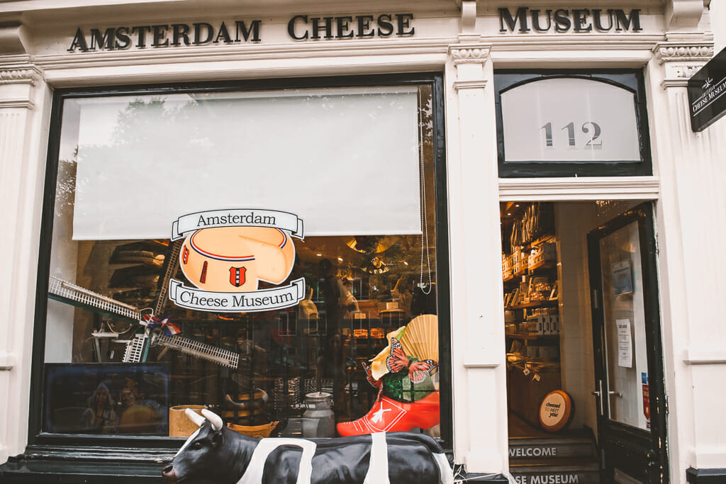 Front window of the Cheese Museum with the door open, white trimming, and a cheese sticker on the window