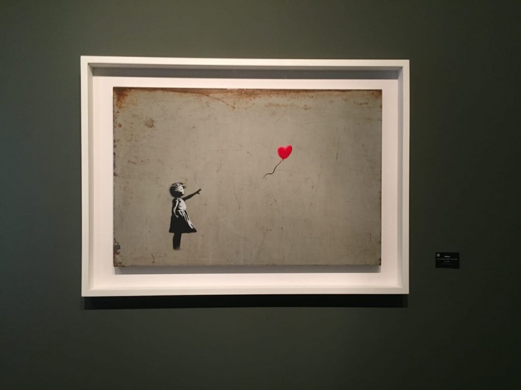 Painting of a little girl in black and white reaching for a red heart balloon thats floating away