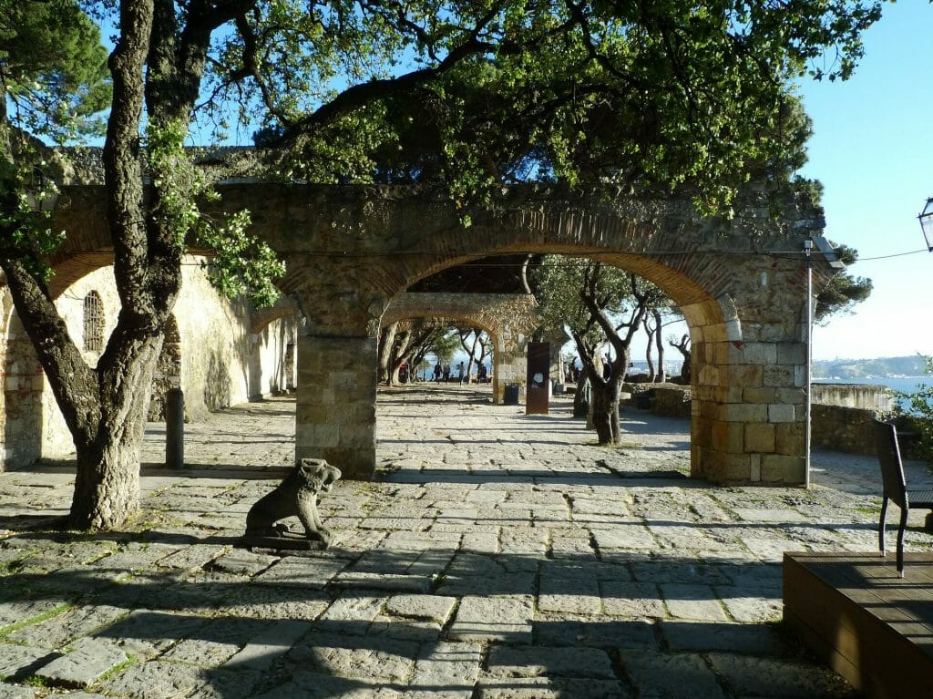 The courtyard of Sao Jorge Castle filled with trees, archways, and lion statues all around