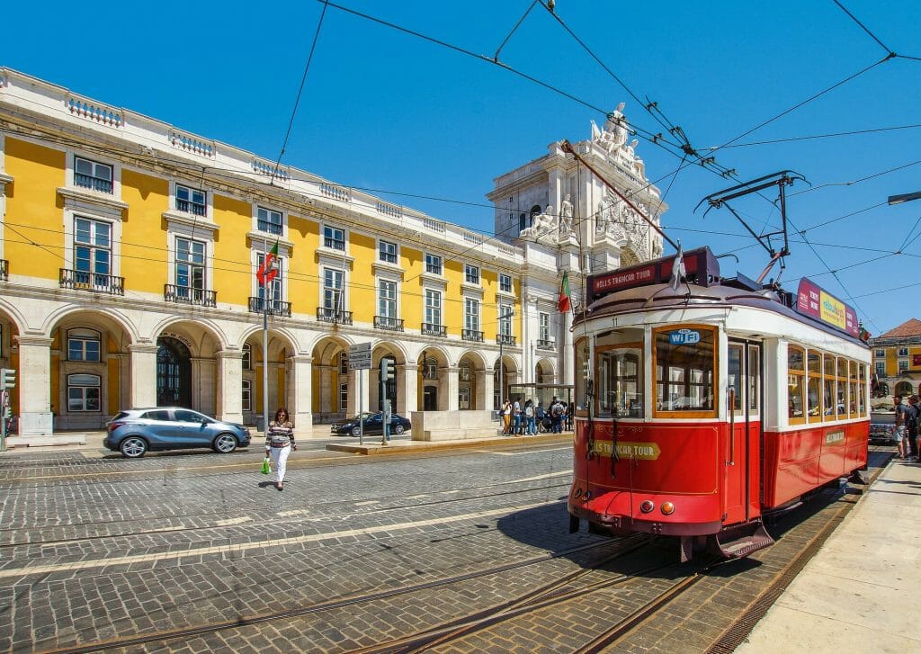 Sunny day in Lisbon with the trolley coming up the street and passed a yellow building