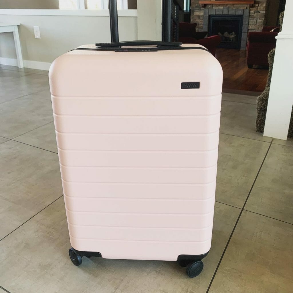 Pink hard shelled carry on on a tiled floor, ready for travel