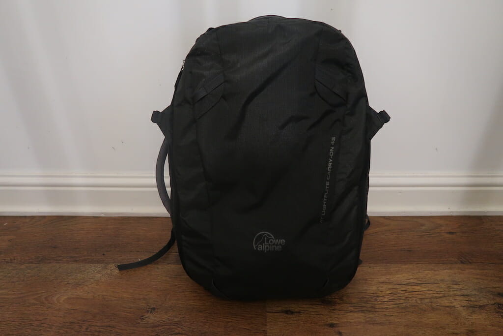 Black carry on backpack resting against a white wall on a lovely wood floor