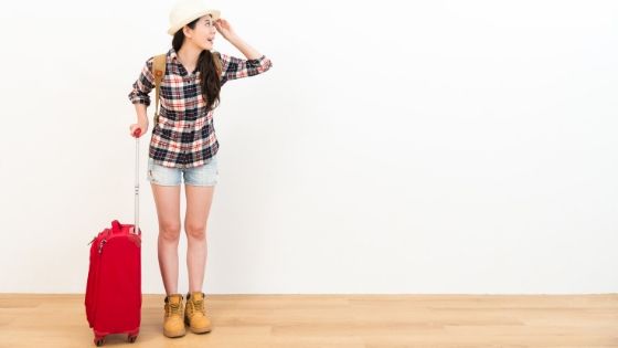 Woman standing in front of white wall with red carry on luggage