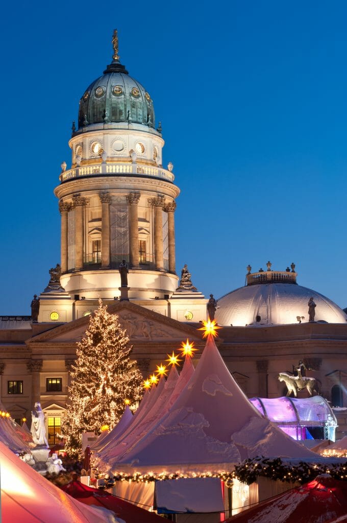 Snow covered white tents in front of a German cathedral in the evening surrounded by twinkling lights