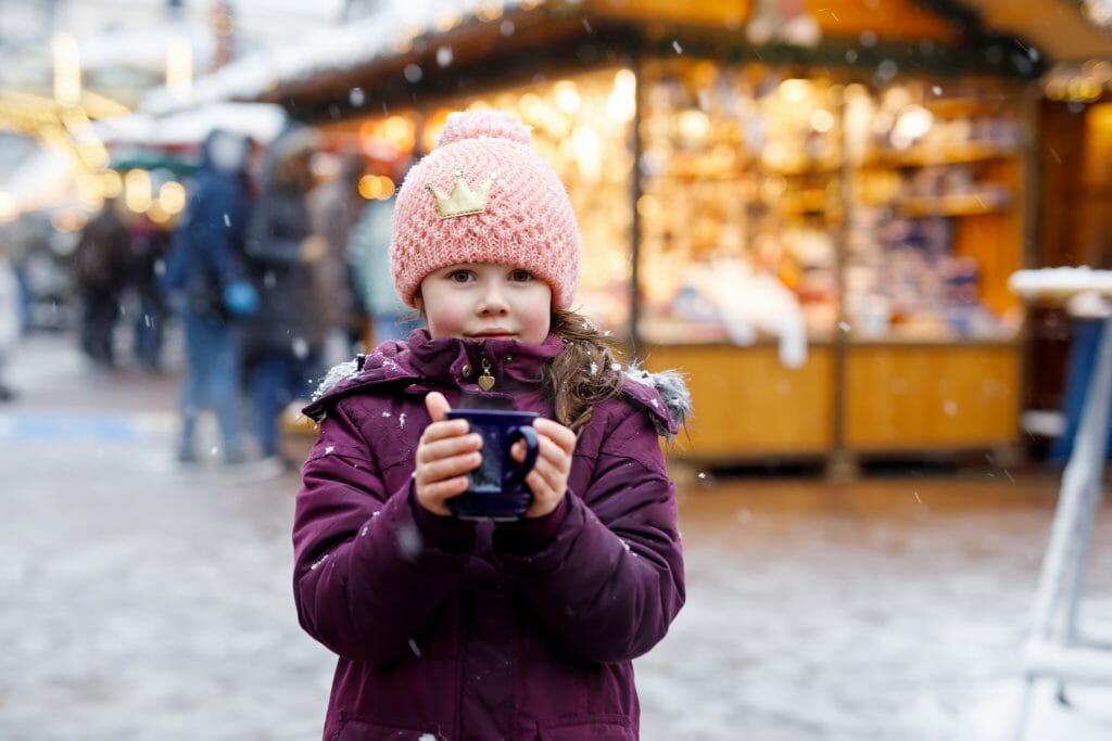 Little cute kid girl with cup of steaming hot chocolate or children punch. Happy child on Christmas market in Germany. Traditional leisure for families on xmas