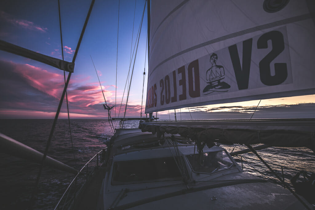 Sailboat SV Delos at sunset with pink/purple/blue sky and clouds