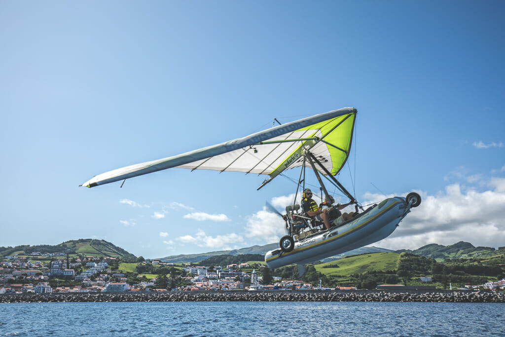 a Dinghy boat with a sail and motor flying over the coast line of Faial Island