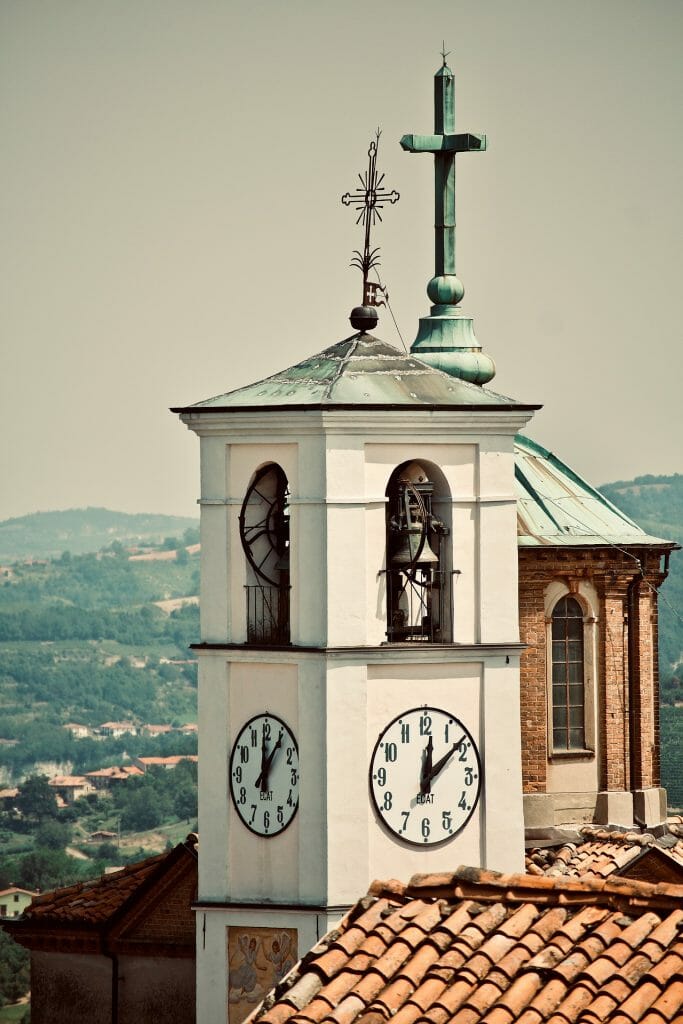 Clock tower overshadowing bell tower with its stark white color and tower cross