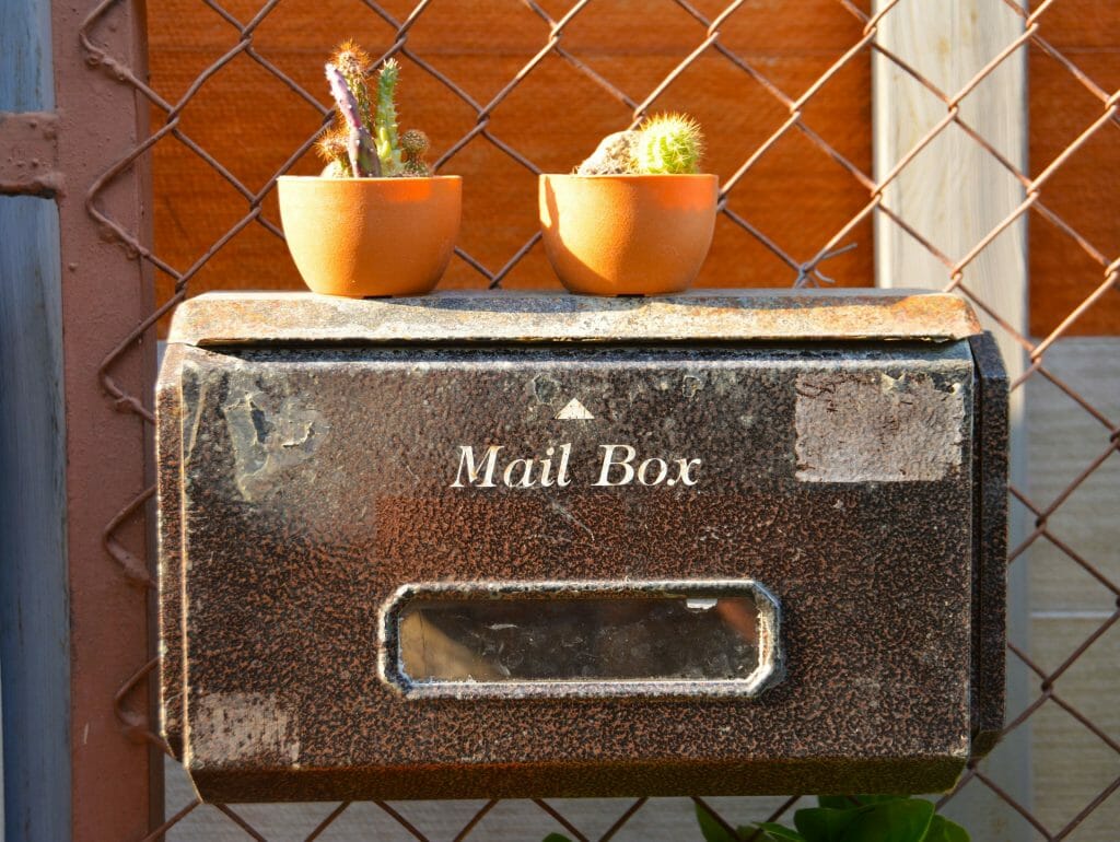 Rusted mailbox in the sun with mini succulents attached to a chain linked fence