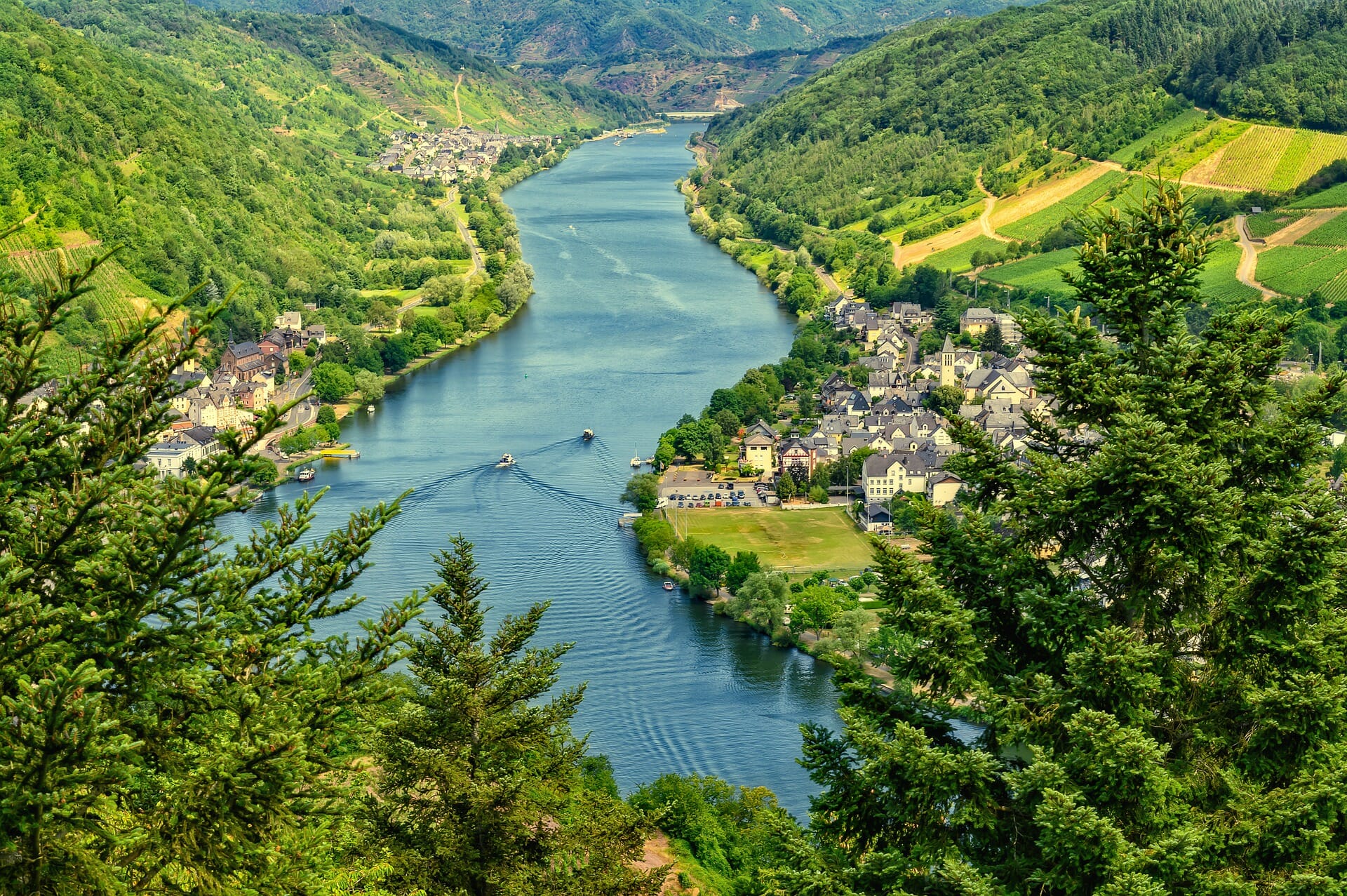 View of the Mosel river in Germany with boats sailing and vineyards being tended to while homes rest comfortably near the water