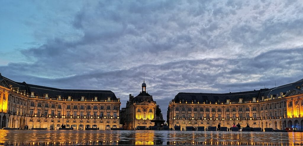 Sun setting into the evening sky behind the water reflecting the gorgeous giant Place de la Bourse