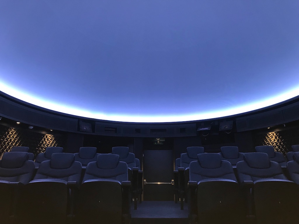 A blank white sky is highlighted by a bright white light outline over chairs in a cruise ship planetarium