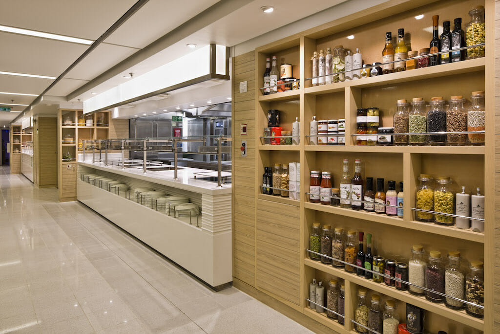 A brightly lit room with shelves filled with spices and food while a cafeteria-like bar awaits customers