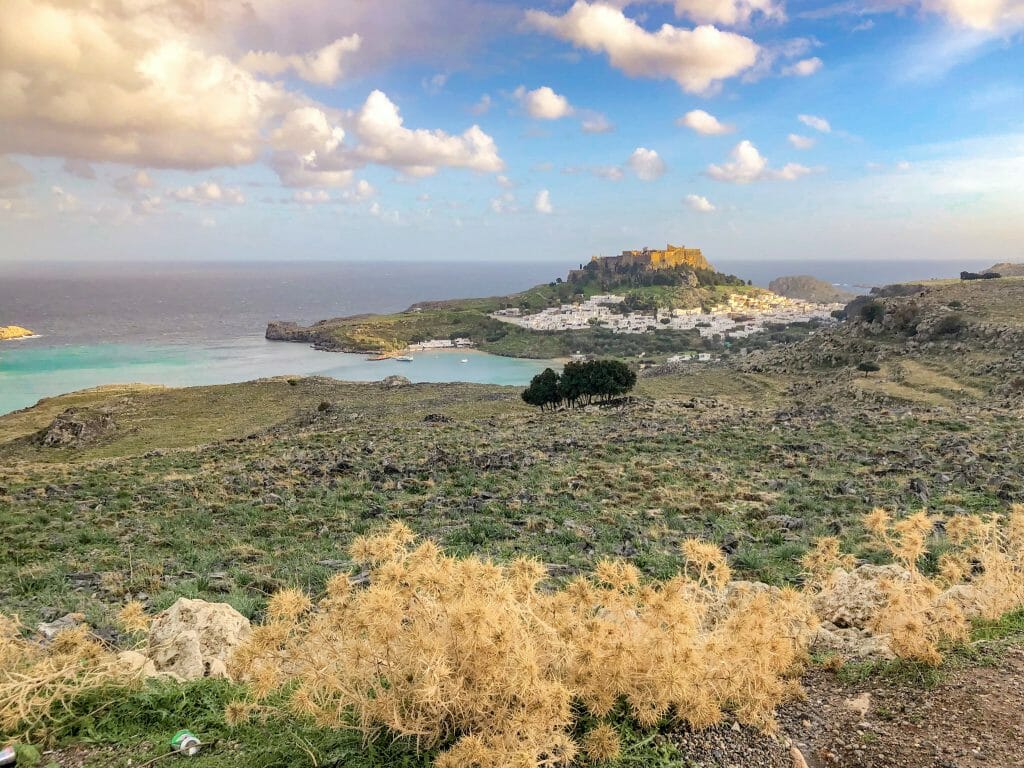 View at Lindos from a distance, with turquoise water to the left and the acropolis sitting on top of the mountain overlooking lindos and the ocean
