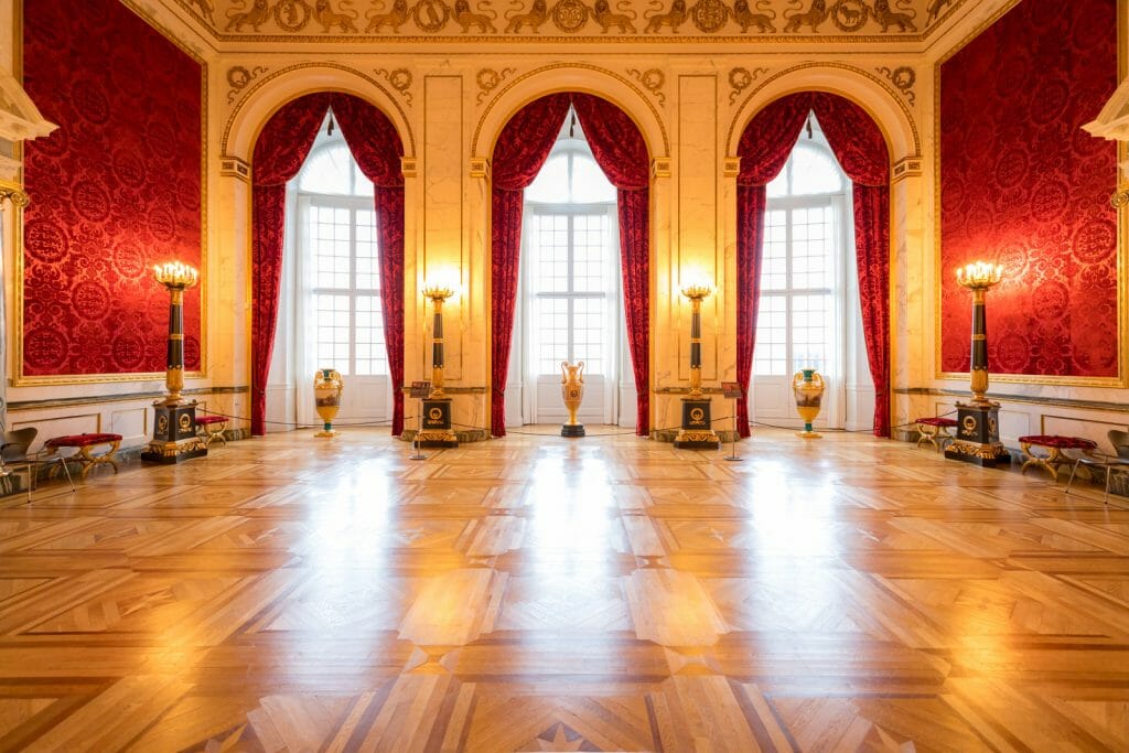 Large ball room with three tall windows with red curtains at the Danish Parliament also known as Christiansborg Palace in Copenhagen Denmark