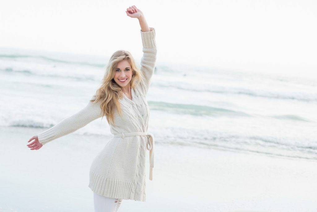 Woman dressed in white cardigan and white pants dancing on the beach