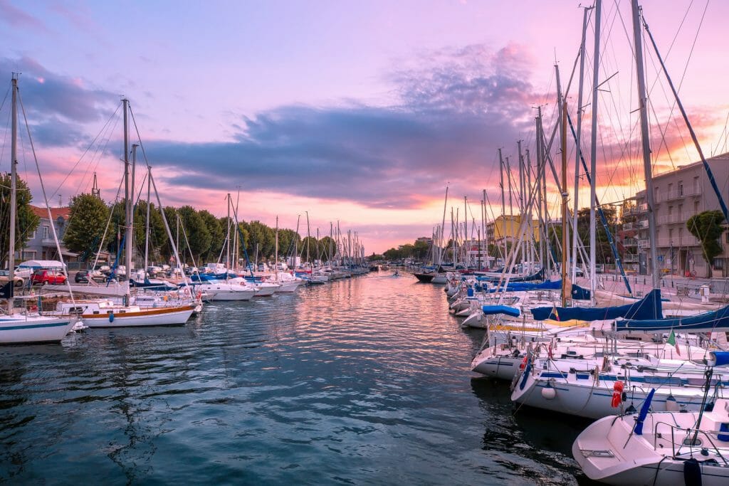Rimini. Italy. Sea boats in marina at the sunrise. Purple sky over Rimini cityscape in summer.
