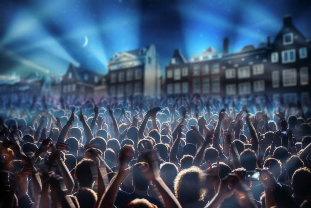 Large crowd of people dancing in the streets of Amsterdam during the night with laser show in the sky above