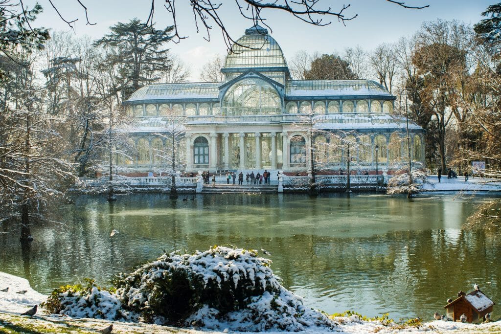 Crystal Palace, a historic glass house in front of a lake in Retiro Park on a snowy day, Madrid Spain