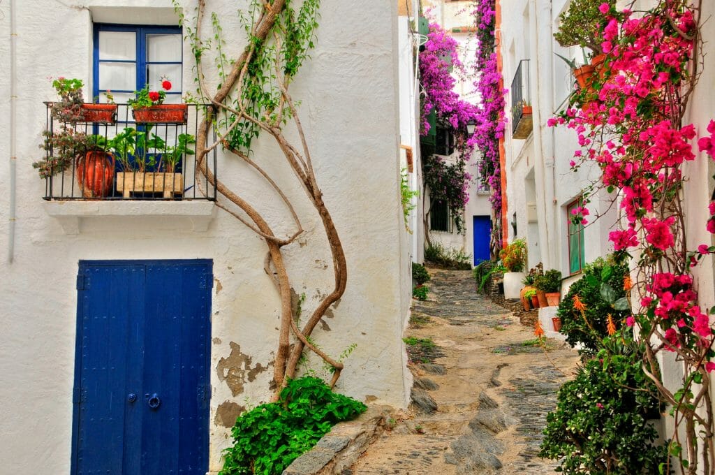 View of a street with white houses, blue doors and shutters and pink bougainvillea in Cadaques, Costa Brava, Spain