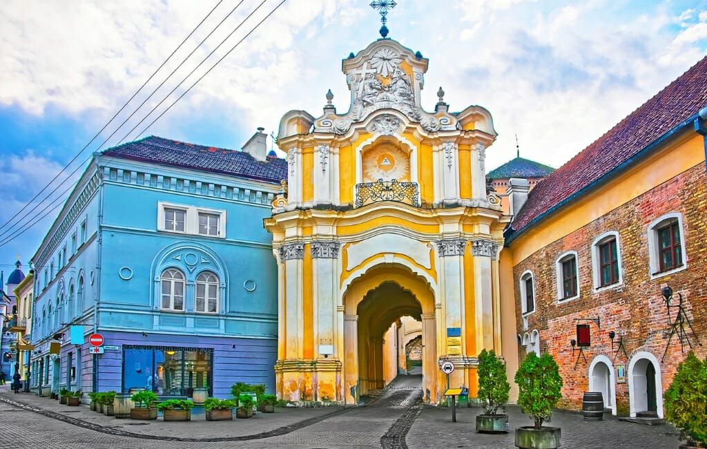 Ornate yellow and white gate house to a monestary next to bright blue and orange building