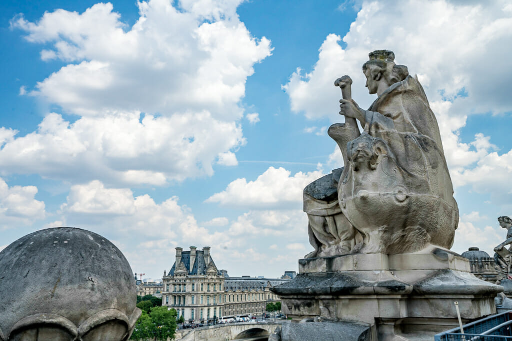 Stone sculpture on the roof of Musée d'Orsay with view of the Louvre in the background
