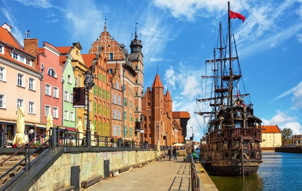 Historic wood sailboat anchored on the waterfront in Gdansk with colorful row houses 