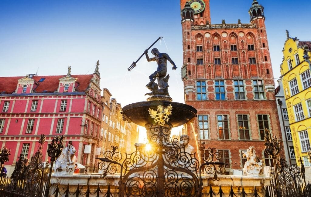 Fountain on the main square in Gdansk with red, orange, and yellow historic buildings in the background