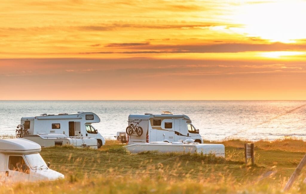 3 white RVs parked by the ocean during sunset