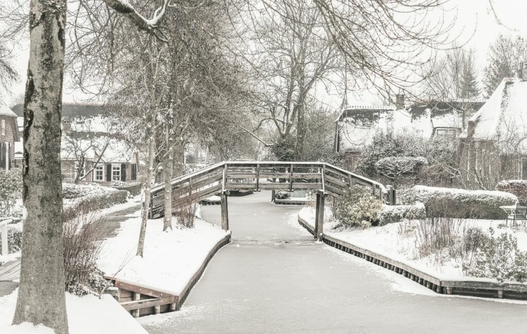 Giethoorn in Winter with snow - canal with wooden bridge and historic houses covered with a blanket of snow