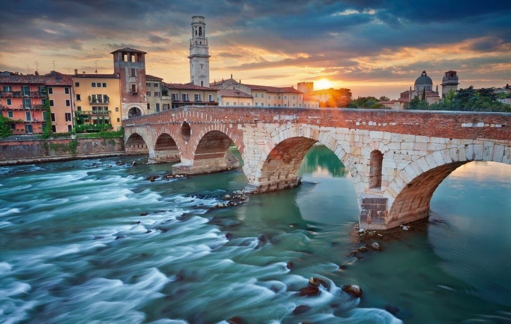 long exposure photo of river in Verona with arched bridge and city of Verona in the background during sunset