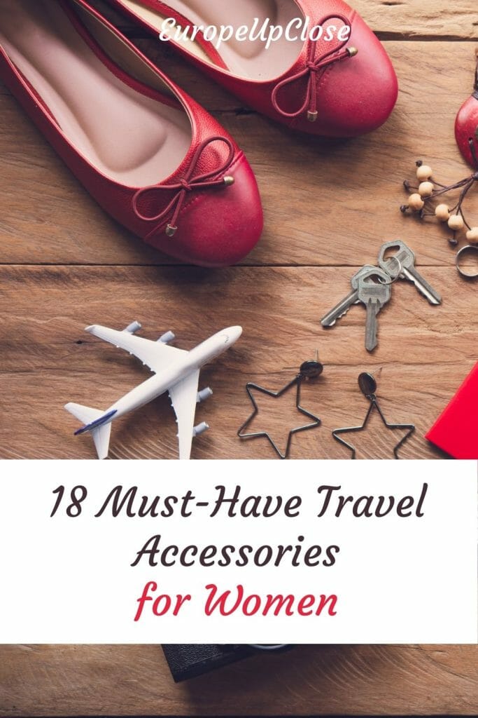 Flatlay with travel accessories for women, including red purse and shoes, camera, small model airplane, sunglasses, hat, camera, jewelry etc, with text overlay on white background: 18 Must Have Travel Accessories for Women - This list of 18 must-have travel accessories for women is perfect if you are looking for fun travel themed gifts or want to treat yourself.