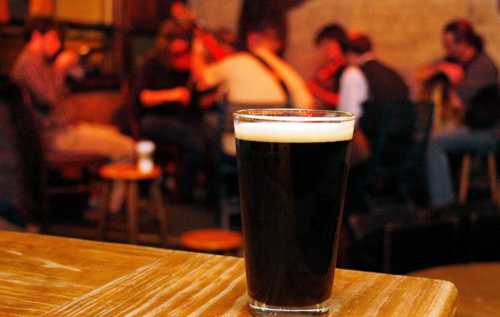 Pint of dark beer in the foreground on table, people out of focus on tables in the background
